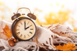 Alarm clock, acorns, scarf and autumn leaves on table outdoors. Daylight saving time end
