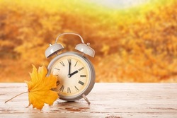 Alarm clock and autumn leaf on table outdoors. Daylight saving time end