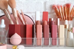 Organizer with decorative cosmetics and makeup brushes on table near white brick wall, closeup
