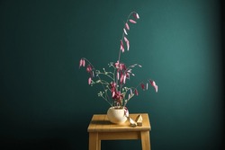 Pot with beautiful ikebana on stool near color wall