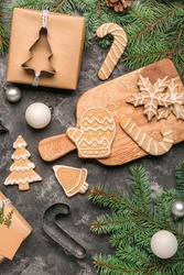 Wooden board with tasty Christmas cookies, gift and fir branches on dark background