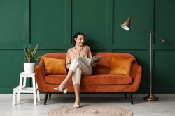 Young woman reading magazine on red sofa near green wall