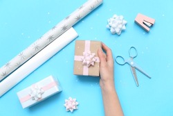 Woman with gift box, bows, scissors, stapler and wrapping paper on blue background