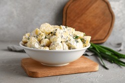 Bowl of tasty Potato Salad with greens on grey background