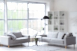 Blurred interior of light living room with grey sofas, coffee table and big window