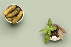 Bowls with pickled cucumbers and different spices on green background