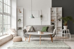 Interior of light living room with grey sofa, coffee table and big window