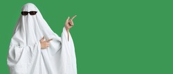 Person in costume of ghost pointing at something on green background with space for text. Halloween celebration