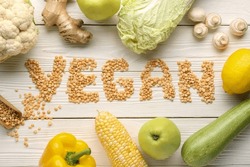 Word VEGAN made of dried peas and different fresh vegetables on white wooden background