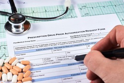 Human fill Prescription drugs prior authorization request form, pills, stethoscope on a EKG graph paper background. Close-up.