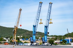Heavy lifting tower mobile crane for loading cargo in the small commercial sea port with moutain view in the background.
