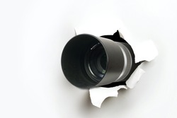 Concept of paparazzi or hidden camera, camera lens looks out through a hole in white paper wall