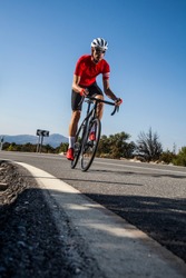 Young cyclist with red jersey and black bike climbs up a road with his gravel bike