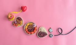 Organic  healthy  food  in  wooden  bowls ,medical  stethoscope , red  heart  shape  and  yellow  tape  measure  wrapped  around  the  apple  on  pink background  for the  health  concept .Top  view. 