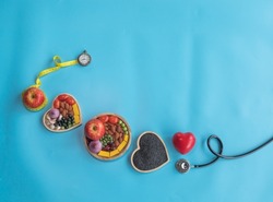 Organic  healthy  food in  wooden  bowl ,medical  stethoscope  ,red  heart  shape  and  yellow  tape  measure  wrapped  round  the  apple  on  blue  background  for  the  health  concept.
Top view.
