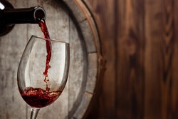 red wine pouring from bottle into glass with old wooden barrel as background