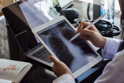 Female doctor hand holding digital tablet with chest x-ray film (CXR ) on screen and work on laptop computer at the office in clinic or hospital. Medical and health care concept.