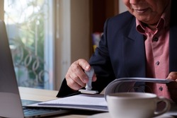 Senior asian business man hand stamping rubber stamp on document in folder with laptop computer and cup of coffee on the desk at office. Authorized allowance permission approval concept.
