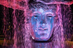 Fountain - a stone face in a Greek park in streams of water at night.