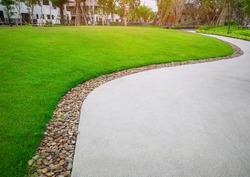 Green grass lawn and gray curve pattern walkway, sand washed finishing on concrete paving with brown gravel border, trees with supporting and shrub in a good care maintenance landscape and garden