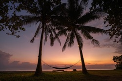 the morning light in shade of purple and orange shine bathe the sky before sunrise with a silhouette of cradle tied with two coconut trees to rest and relax