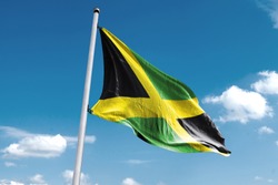 Waving Flag of Jamaica in Blue Sky. Jamaica Flag on pole for Independence day. The symbol of the state on wavy cotton fabric.