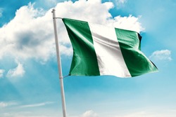 Waving Flag of Nigeria in Blue Sky. Nigeria Flag on pole for Independence day. The symbol of the state on wavy cotton fabric.