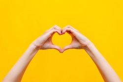 Female hands showing a heart shape isolated on a bright
color yellow background. Sign of love, harmony, gratitude, charity. Feelings and emotions concept