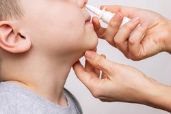 A close-up of female hands using nasal spray for a child's runny nose and congestion isolated on a white background. Treatment of the disease. Rhinitis, sinusitis, cold, flu. A mother treats her kid