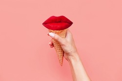 Ice cream waffle cone with red lips inside in a female hand isolated on a color pink background. Trendy creative conceptual collage in magazine style. Contemporary art. Modern design. Summer concept