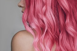 Close-up of the wavy pink hair of a young woman isolated on a gray background. Result of coloring, highlighting, perming. Beauty and fashion
