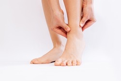 Cropped shot of a young woman touching painful twisted or broken ankle with her hands isolated on a white background. The girl twisted her leg. Sport injury, painful sprained ankle muscle