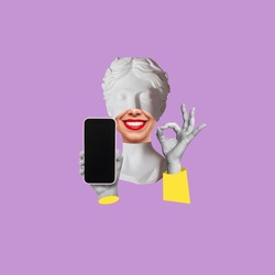 Young smiling woman headed by antique statue holds mobile phone with blank black screen with copy space for text or design showing the ok gesture isolated on purple color background. Contemporary art