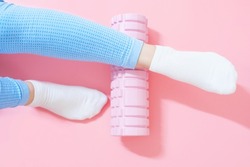 Female leg rolls a massage foam roller close-up on a pink background, top view.