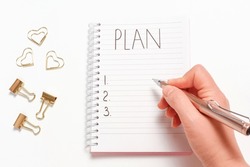 Female hand writes plan in a notebook on white background close up.