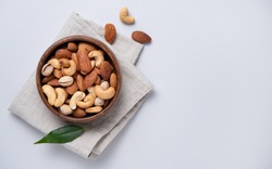 almonds, pistachios and cashews are placed in a wooden bowl on a linen napkin on a light grey background. Top view and copy space. Horizontal orientation