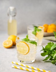 Lemonade soda drink with fresh lemons. Refreshing cocktail with lemon, mint and ice on textured light background. Summer cold drinks concept.