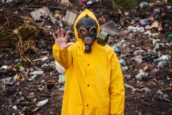 Man in overalls and gas mask shows a gesture to stop. In  background garbage dump. Concept of human pollution