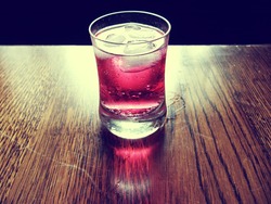 Refreshing cold red soda drink with lots of ice. Soda drink in a small glass. Soda drink is transparent and bubbles can be seen. A red reflection can be seen on the wood. There is a black background.