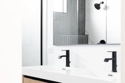 A beautifully renovated bathroom with a wood vanity cabinet, black marble herringbone tiles in the shower, and a white countertop with black faucets. Detail shot.