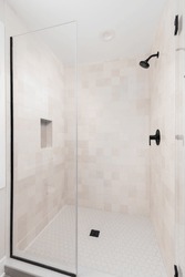 A shower with brown square tiles, black showerhead, and a hexagon tile floor.