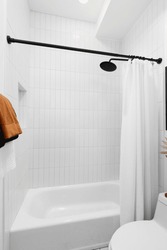 A shower with white vertical subway tiles, black showerhead and curtain road, and orange towels.