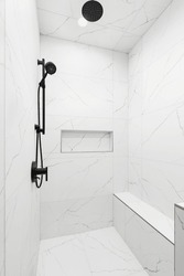 A luxury shower with white marble walls and floor, a black faucet and showerhead, and a marble niche shelf.