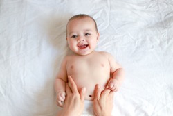 Adorable newborn baby boy with smiling face top view relaxing time doing belly massage by his mother. Mixed race Asian-German infant massaging and laughing.