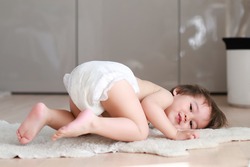 Adorable baby boy wearing diaper lying on his stomach on the ground with smiling face. Happy mixed race Asian-German infant playing and relaxing at home. Cute and funny kid.