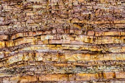 closeup of an ancient brown cracked, finely layered limestone cliff