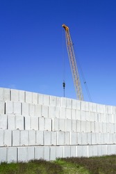 Large concrete cube block stacks in the backyard of a concrete product plant against a blue sky and yellow crane boom background