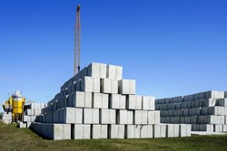 Large concrete cube block stacks in the backyard of a concrete product plant against a blue sky and yellow crane boom background