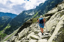 Trekkers climb in the mountains. Woman with sticks and backpack  are walking on a stone path in mountain. Tourist on a trip in mountain. Extreme mountains travel. Landscape in Tatras.