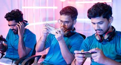 Team of young professional gamers playing live video game on mobile phone by talking on headphones at esports league
